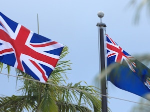 Cayman Islands and Union Jack flag on poles in between palm trees on the Cayman Islands