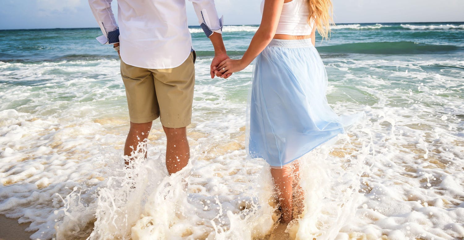 Couple holding hands while wading through the water on the beach