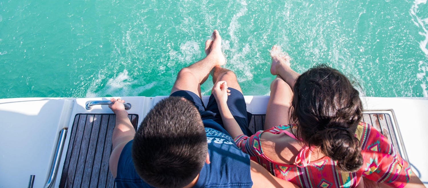 Couple sitting with feet hanging in the water off the edge of a boat