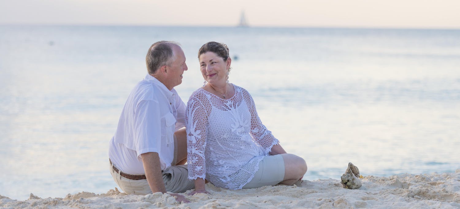 Elderly couple staring into each others eyes while sitting on the beach