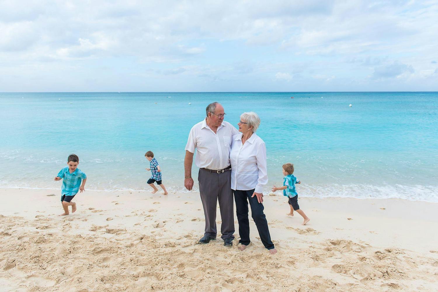 Elderly couple with 3 children running around them on the beach