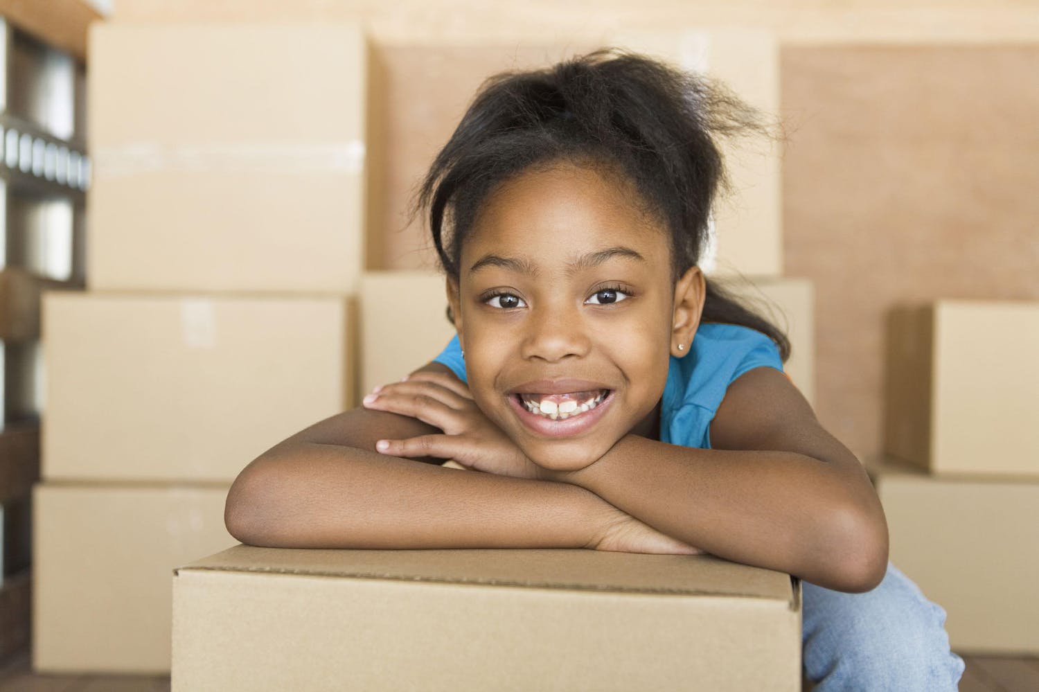 Young girl smiling and leaning on moving box in a room full of boxes