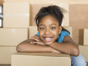 Young girl smiling and leaning on moving box in a room full of boxes