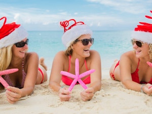 Three ladies laying on the beach wearing Santa hats and holding fake starfish