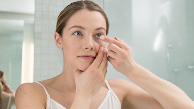 Woman Holding contact lens to eye looking in mirror