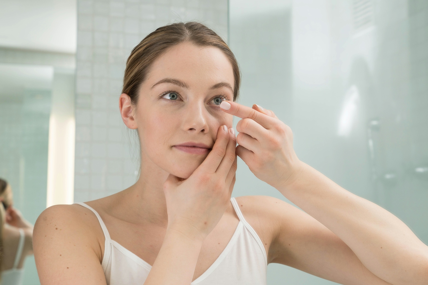 Woman Holding contact lens to eye looking in mirror