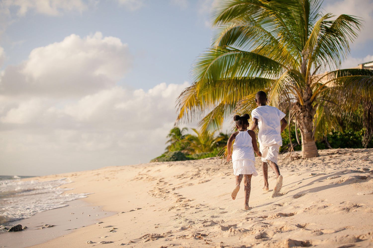 Young girl and boy dressed in white running on the beach