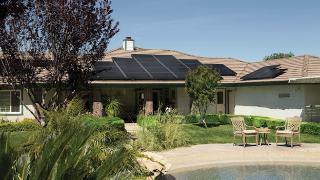 Black solar panels on brown roof of house with pool