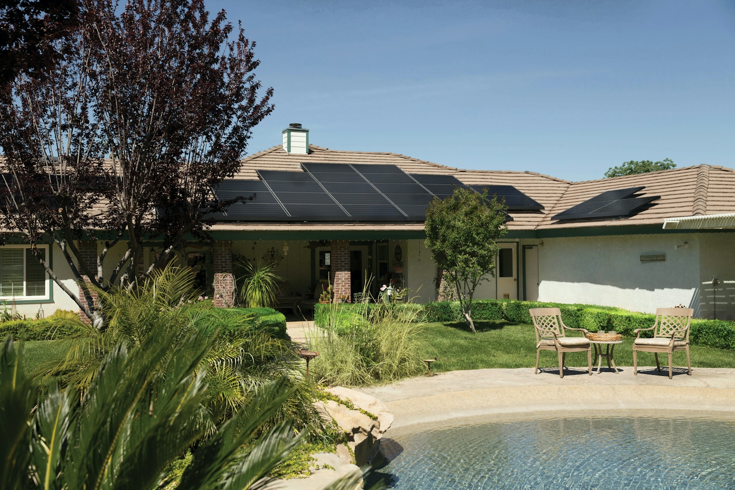 Black solar panels on brown roof of house with pool
