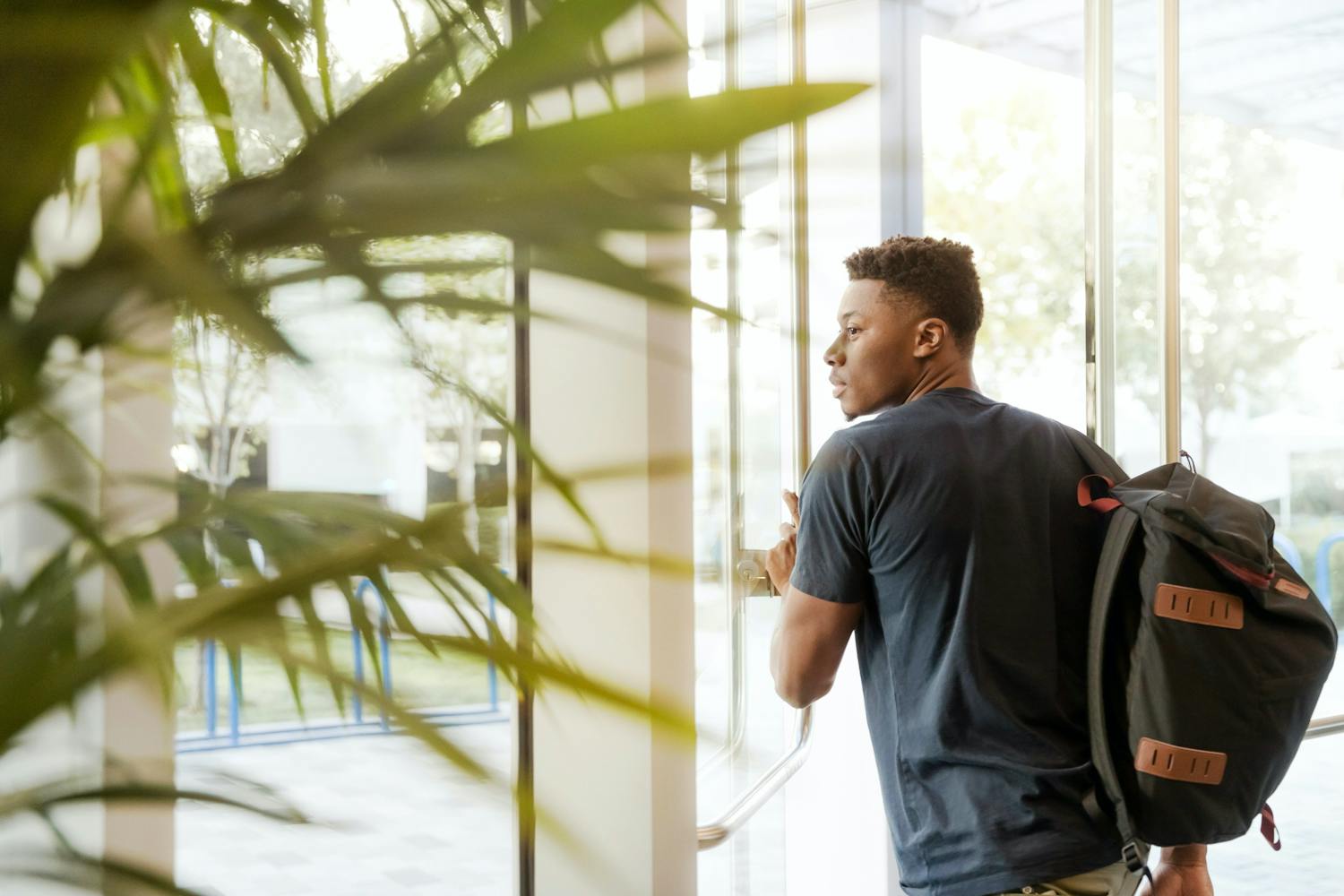 Man looking outside window carrying black and brown backpack