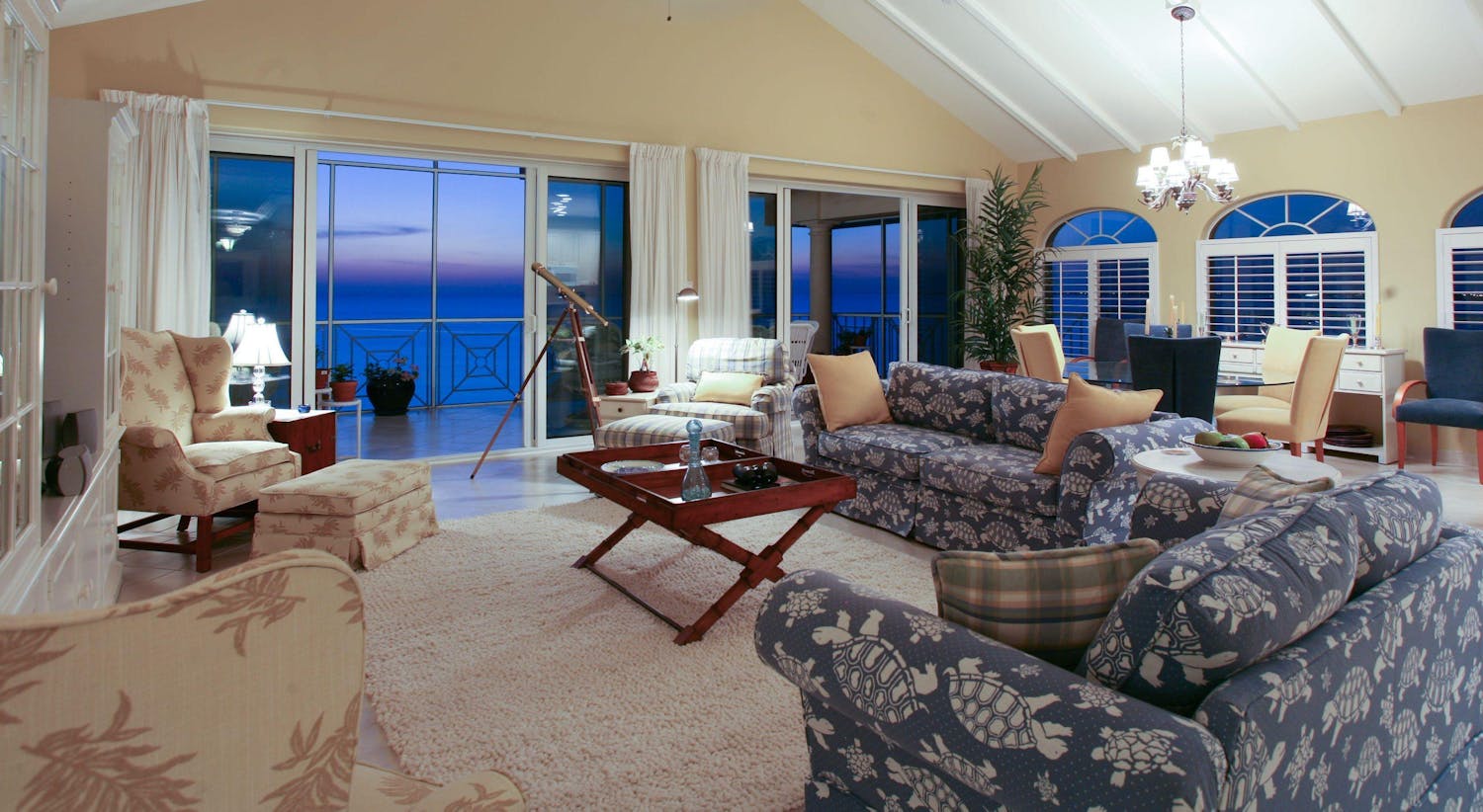 Neutral coloured tropical patterned livingroom furniture gazing over the ocean at dusk
