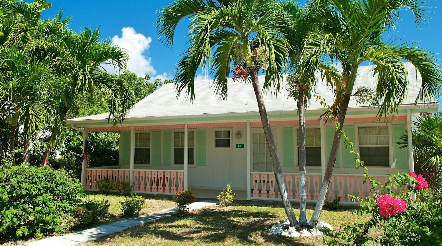 Quaint mint green traditional cayman cottage with veranda and pink blossom trees