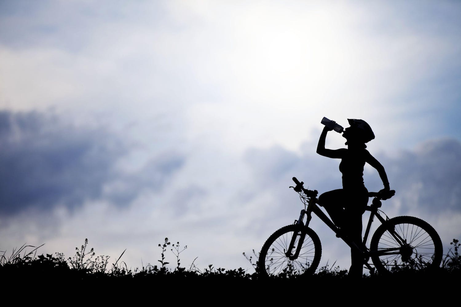 Silhouetted woman drinking water on a bike