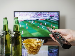 Two beers on a coffee table as a person watching sports holds the remote
