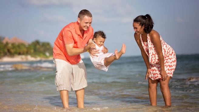 Two parents and child dressed in pink play at the beach