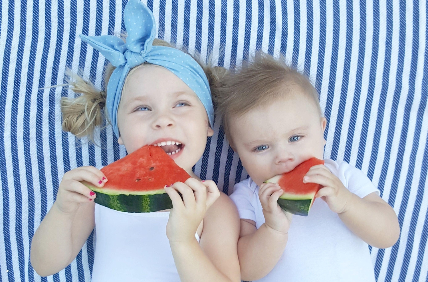 Two young children eating watermelon on a striped blanket