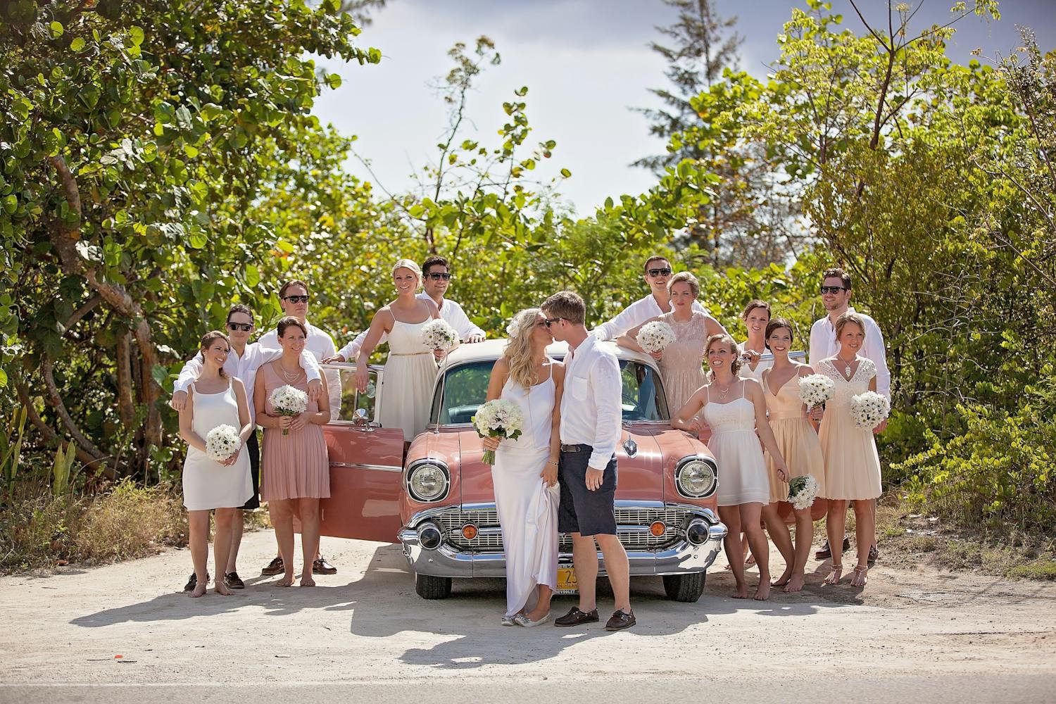 Wedding party sitting in front of pink classic car