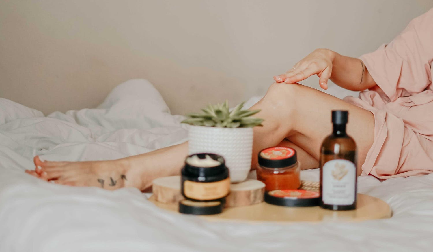Woman with holistic beauty products lounging on a bed with only leg visable